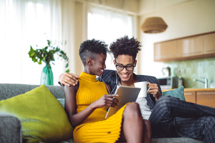 A couple ona. sofa reading about Lottery betting vs Sports Betting on their tablet