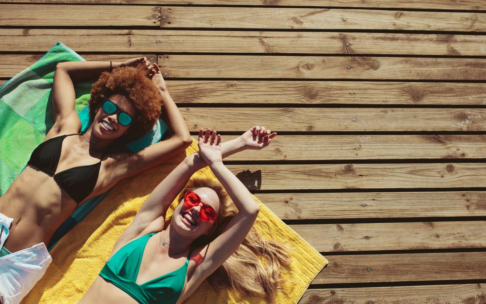 Two South African women sunbathing on a wooden floor after playing the France Lotto online