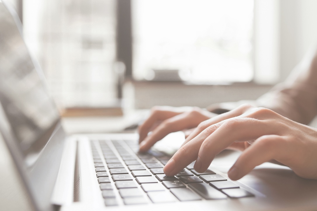 A cllose up of a womans hands typing on a laptop's keyboard, checking whether or not it is safe to bet on the lottery online